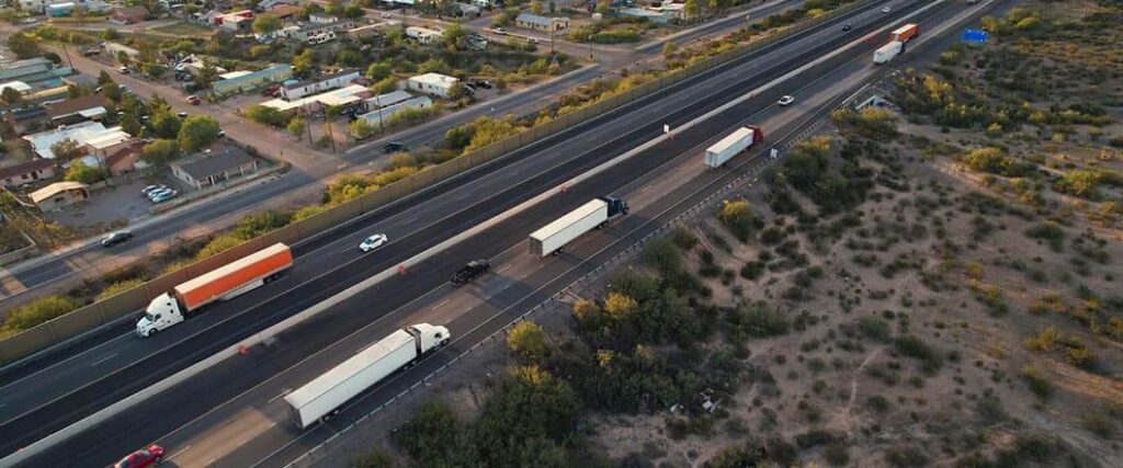 An overhead view of several semi trucks traveling in a convoy on a highway. 